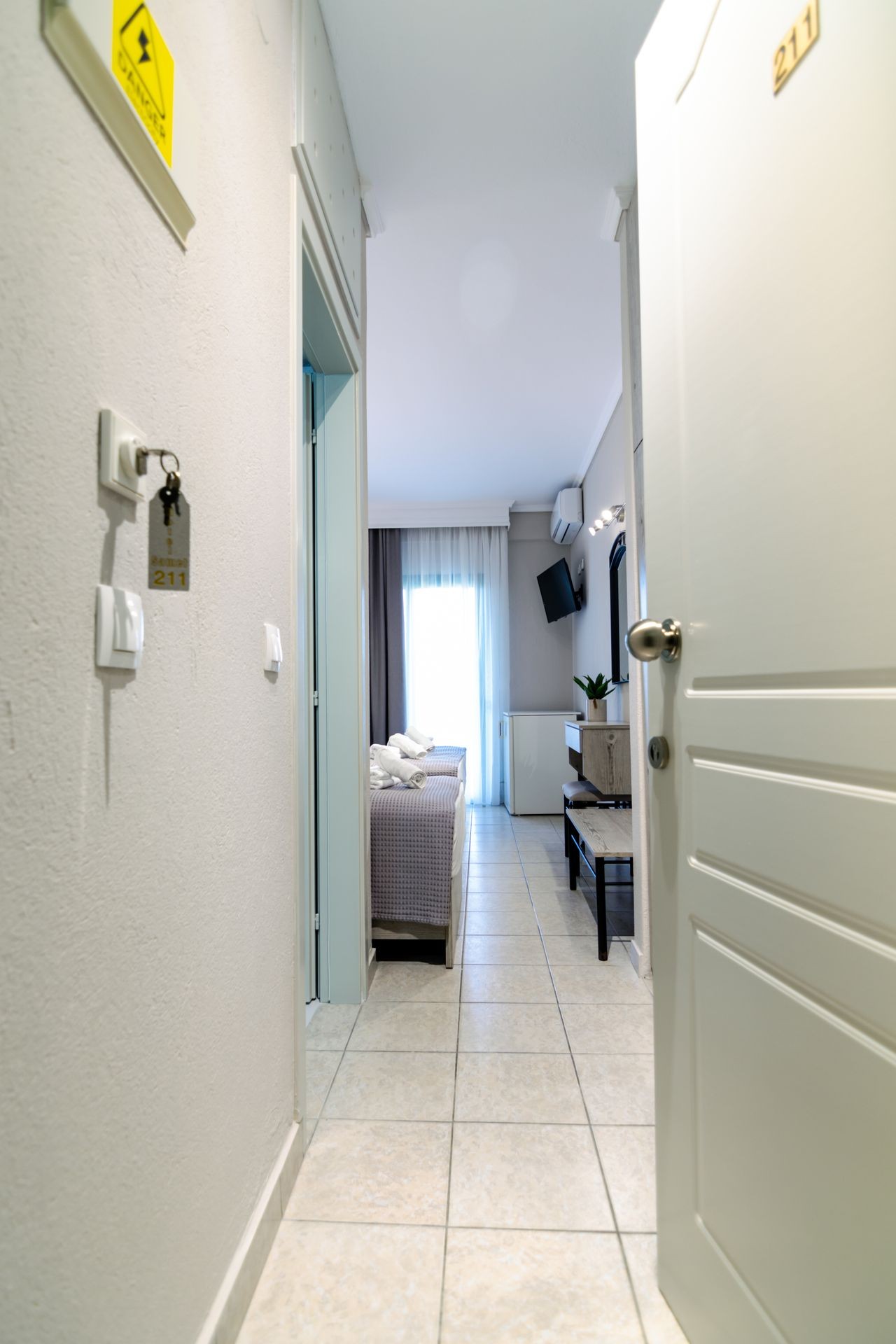 Open door revealing a hotel room with tiled floor, bed, TV, and balcony access.