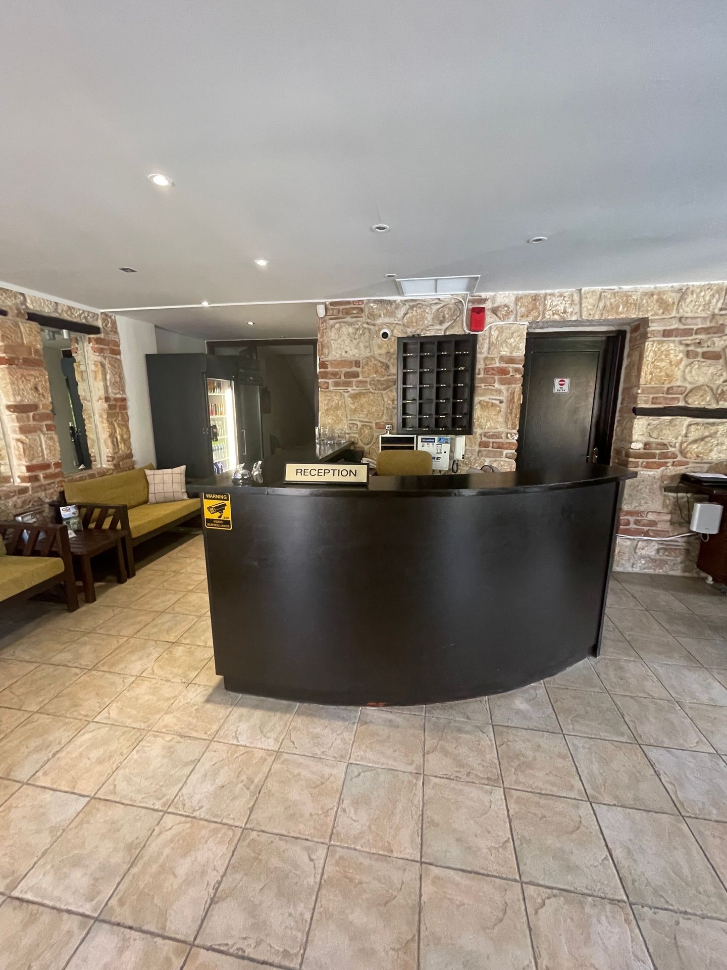 Hotel reception area with a curved black desk, stone walls, tiled floor, and seating area.